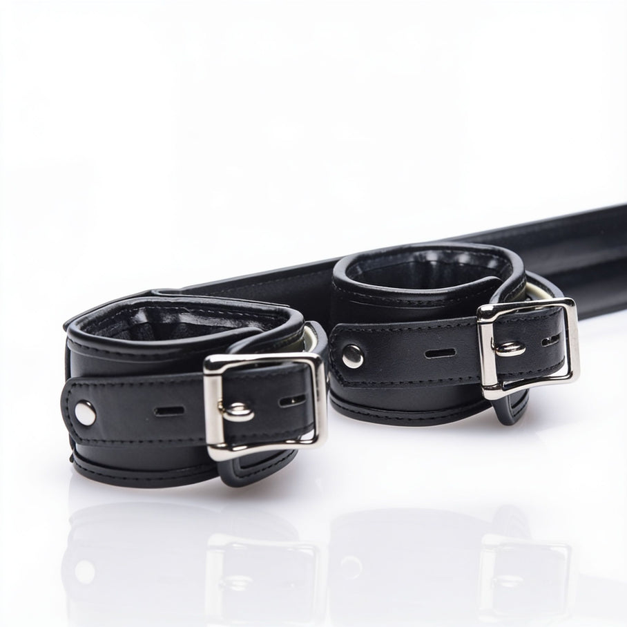 Close-up of the Deluxe Rigid Spreader Bar showing padded faux leather cuffs, reinforced stitching, adjustable buckle closures, and polished metal hardware